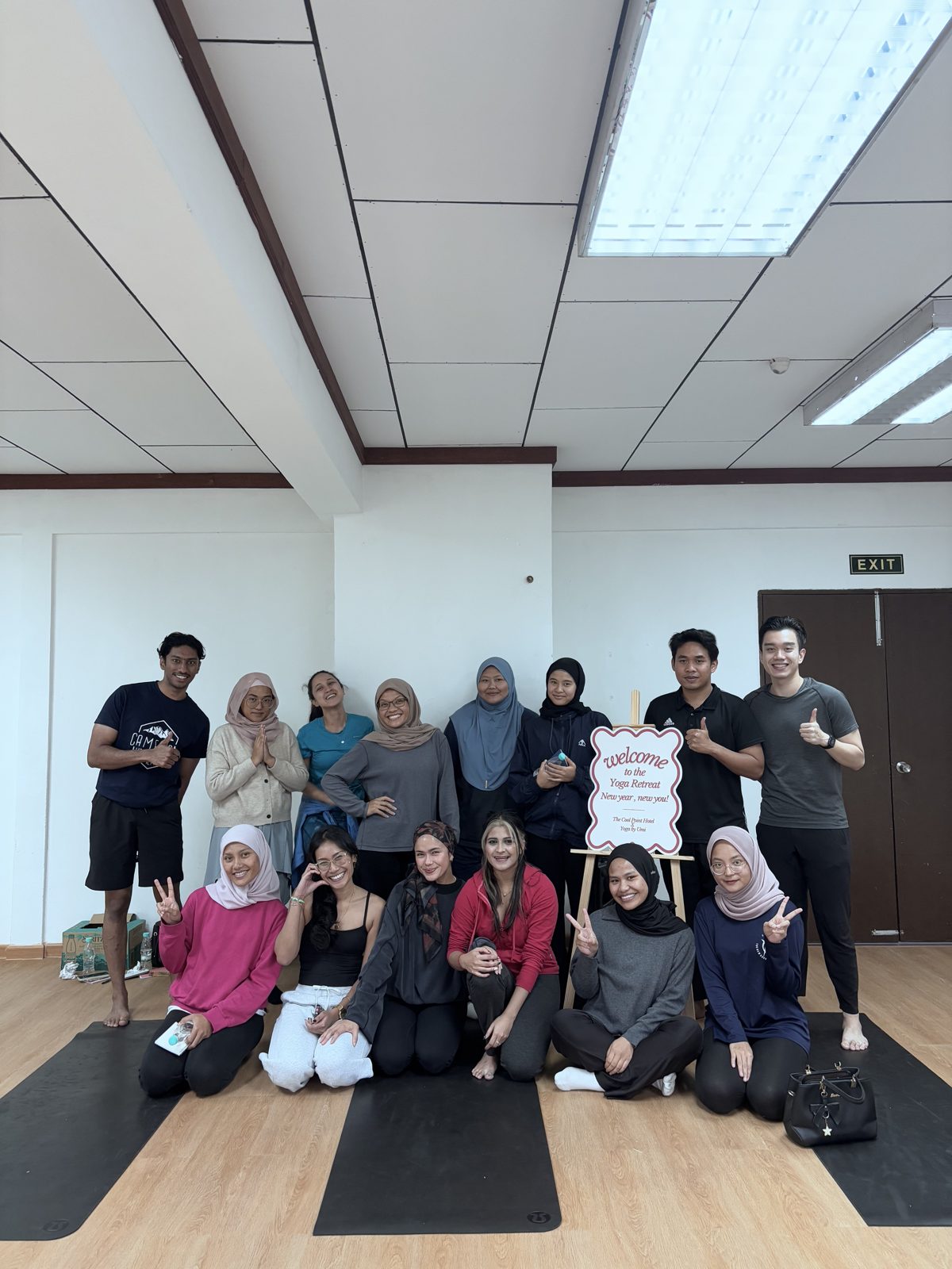 Guests and hosts of the January 2025 Yoga Retreat at The Cool Point Hotel, posing on mats beside the welcome sign