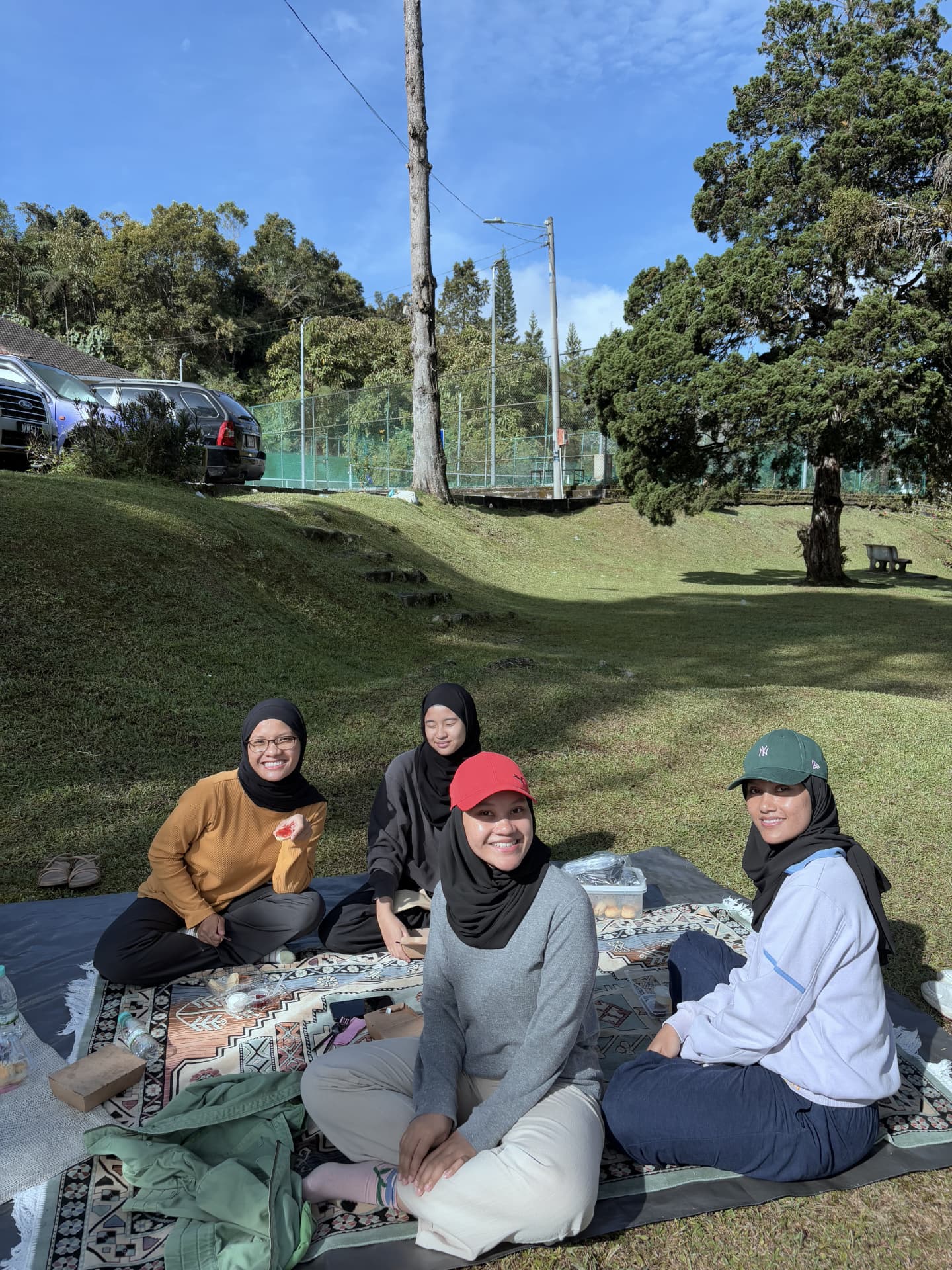 Four guests of the January 2025 Yoga Retreat sharing a picnic on the lawn at The Cool Point Hotel, smiling at the camera
